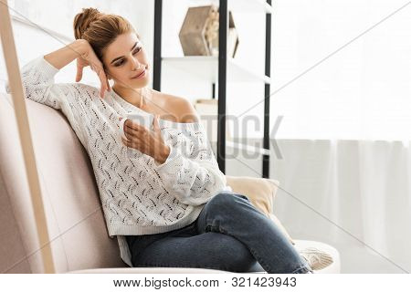 Attractive Woman In White Sweater Holding Cup And Looking Away