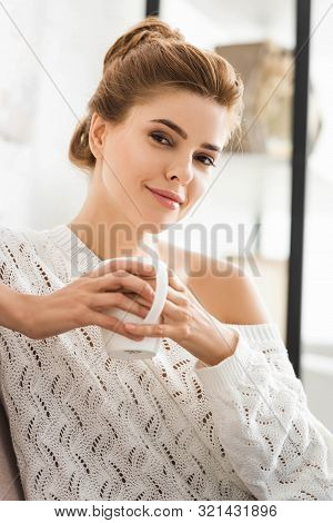 Attractive Woman In White Sweater Holding Cup And Looking At Camera
