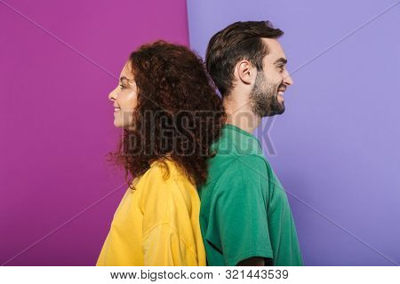 Portrait of young caucasian couple man and woman in colorful clothing smiling together standing back to back isolated over violet background