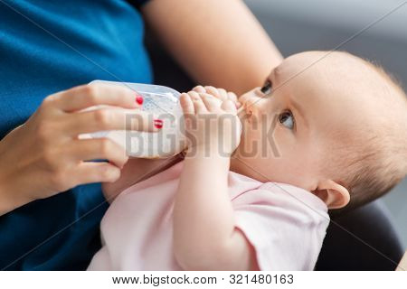 family, babyhood and people concept - close up of mother feeding baby with milk formula from bottle