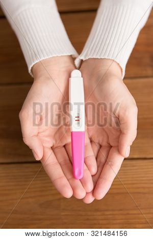 fertility and maternity concept - woman hands holding positive pregnancy test with two stripes over wooden boards background