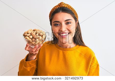 Young beautiful woman holding bowl with peanuts standing over isolated white background with a happy face standing and smiling with a confident smile showing teeth