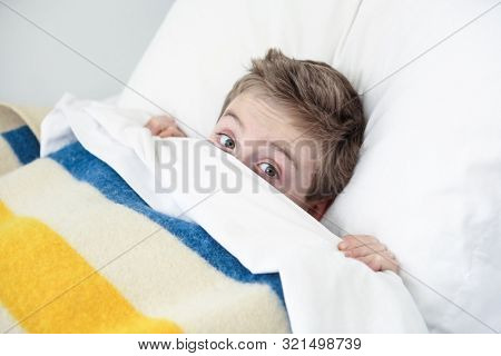 Boy hiding under the covers peeking out