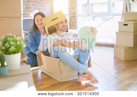 Funny and crazy couple having fun riding a cardboad box as a car, smiling happy and lauging at new home