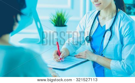 Doctor and patient discussing medical problems in a hospital consulting room. Doc filling in a patient's form