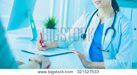 Doctor and patient discussing medical problems in a hospital consulting room. Doc filling in a patient's form