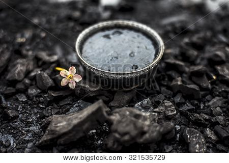 Close Up Of Activated Charcoal In A Glass Bowl On The Wooden Surface Along With Some Raw Powder Of C