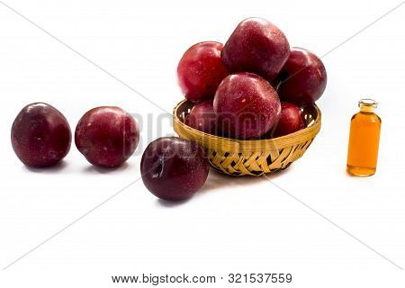 Raw Organic Red Ripe Plums In A Brown-colored Basket Along With Its Extracted Essential Oil In A Sma