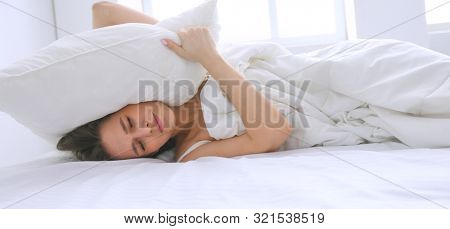 Young caucasian woman covering her head and ears with pillows.