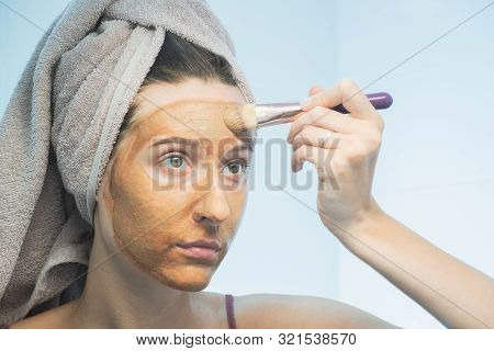 A Young Woman Puts A Clay Mask On Her Face With A Brush In Bathroom. The Concept Of Selfcare, Proper
