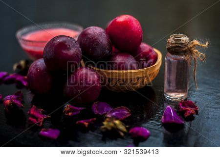 Raw Organic Red Ripe Plums In A Brown-colored Basket Along With Its Extracted Essential Oil In A Tra