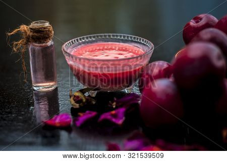 Raw Organic Red Ripe Plums In A Brown-colored Basket Along With Its Extracted Essential Oil In A Tra