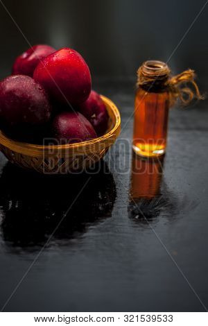 Raw Organic Red Ripe Plums In A Brown-colored Basket Along With Its Extracted Essential Oil In A Tra