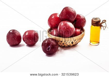 Raw Organic Red Ripe Plums In A Brown-colored Basket Along With Its Extracted Essential Oil In A Tra