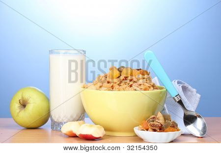 leckere Cornflakes in grüne Schale, Äpfel und Glas Milch auf Holztisch auf blauem Hintergrund
