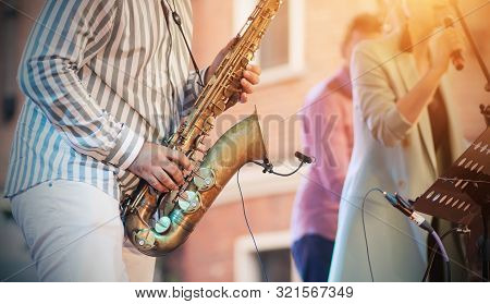 A Skilled Jazzman Plays A Golden Saxophone At A Concert, Creating An Accompaniment To The Singer.