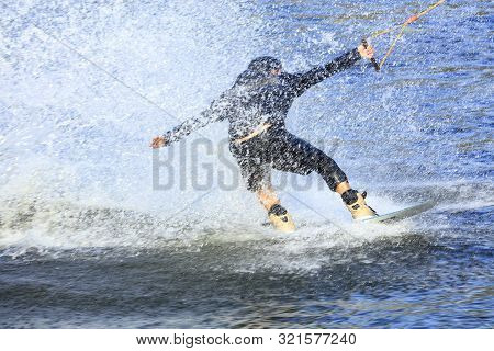 A Wakeboarder Rushes Through The Water At High Speed Creating A Cloud Of Spray Around Himself.