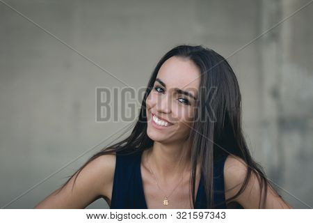 Closeup Portrait Of A Happy Young Brunette Teenage Girl Outdoor. Concrete Wall On Background
