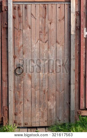Red Wooden Old Door In The Fence With Iron Hinges And A Round Handle. The Paint Is Faded. A Lot Of K