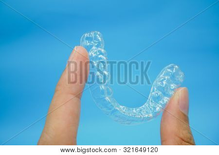 Hand Holding Clear Plastic Retainer Teeth That Isolated On Blue Sky Background. It's An Equipment Fo