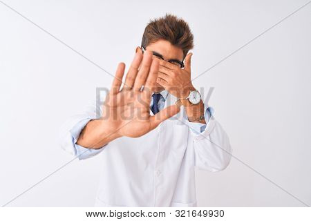 Young handsome sciencist man wearing glasses and coat over isolated white background covering eyes with hands and doing stop gesture with sad and fear expression. Embarrassed and negative concept.