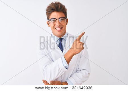 Young handsome sciencist man wearing glasses and coat over isolated white background with a big smile on face, pointing with hand finger to the side looking at the camera.