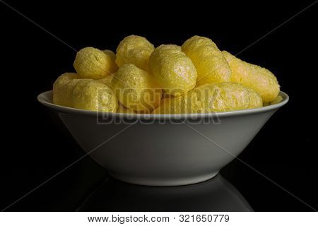 Lot Of Whole Salted Yellow Corn Puff In White Ceramic Bowl Isolated On Black Glass