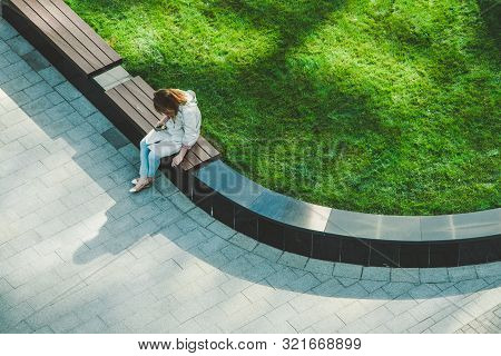 Frustrated Caucasian Woman With The Phone And Cigarette Sitting On The Wooden Bench In The Garden. B