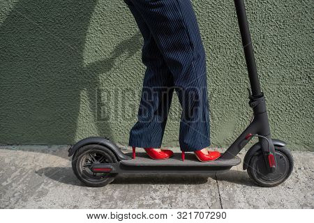 Young Woman In Formal Wear On Red Hight Heels Is Standing On Electrical Scooter. Close-up Of Female 