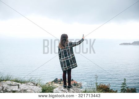 A Tourist Girl Or A Blogger Takes Pictures Or Records Videos Of A Sea View. Or She Takes A Selfie.