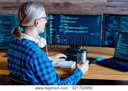 Back View Of Man Freelancer In White Headphones Is Working At Home Office. Programmer Developer Is W