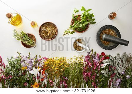 Top View Of Mortars And Pestles With Herbal Blends Near Flowers And Bottles On White Background