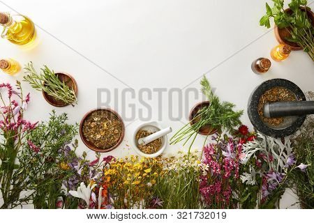 Top View Of Mortars And Pestles With Herbal Blends Near Flowers On White Background