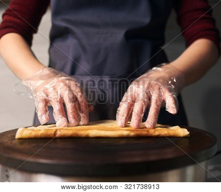 Cropped View Of Professional Cook In Apron While Baking Crepe Process On Hot Round Cooktop. Skillful