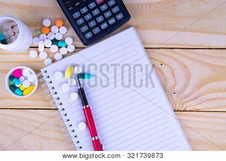 Top View Pen On The Book With White Bottle And Heap Of Pill And Calculator On Wooden Table. Hard Wor