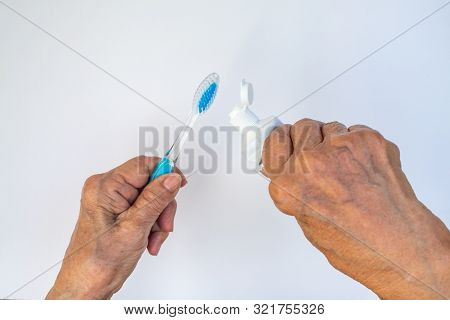 Senior Woman's Hands Squeezing Toothpaste On Brush Against Isolated On White Background