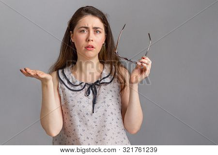 People And Emotions. A Young Brunette In A Blouse, Holding Glasses In Her Hands, Spreads Her Hands I