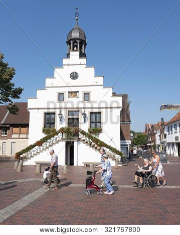 Lingen, Germany, 27 August 2019: Senior Tourists Pass Old Town Hall On Market Square In German Town 