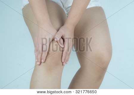 Closeup Young Woman Massaging Her Painful Knee On Grey Background. Healthcare And Medical Concept.