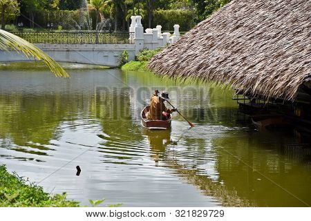 Kanchanaburi, Thailand, 09.09.2019: A Thai Man In Traditional Thai, Siamese Dress Is Rowing An Old T