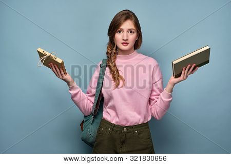 A Girl In A Pink Sweater With A Backpack And Headphones On Her Neck Stands With Her Hands Spread Out