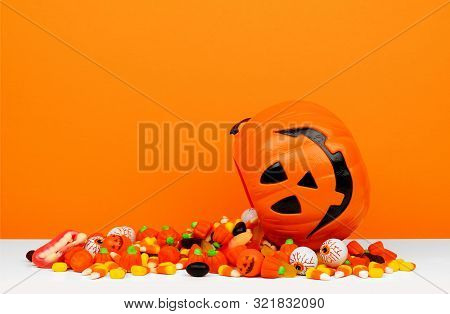 Halloween Jack O Lantern Bucket With Spilling Candy, Side View On An Orange Background
