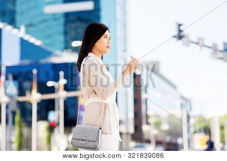 lifestyle and people concept - young asian woman drinking water flom plastic bottle in city