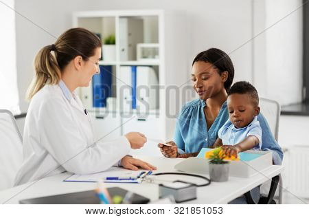 medicine, healthcare and pediatry concept - caucasian doctor giving prescription to african american mother with baby son at clinic