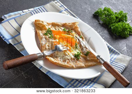 Breton Crepe, Savory Buckwheat Galettes Bretonnes With Spilled Egg, Cheese, Ham On A White Plate On 