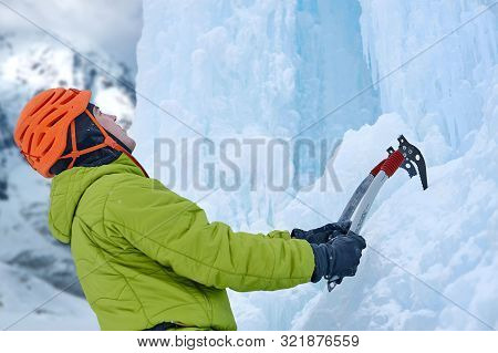 Alpinist Man With Ice Tools Axe In Orange Helmet Climbing A Large Wall Of Ice. Outdoor Sports Portra