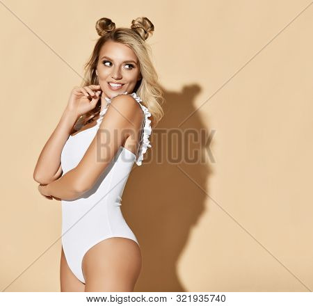 Glamorous And Sexy Blonde Woman With Funny Buns And Brilliant Smile In White Bodysuit Looks Back Ove
