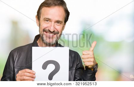 Handsome middle age man holding paper with question mark happy with big smile doing ok sign, thumb up with fingers, excellent sign