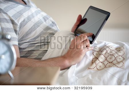 Læse en digital tablet i seng mand holder og at røre ved skærmen
