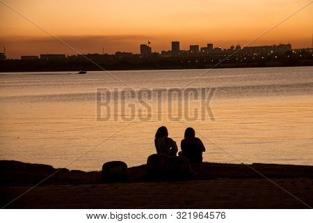 Two Ladies Watching The Sunset Over Brasilia, Brazil, From Lake Paranoa